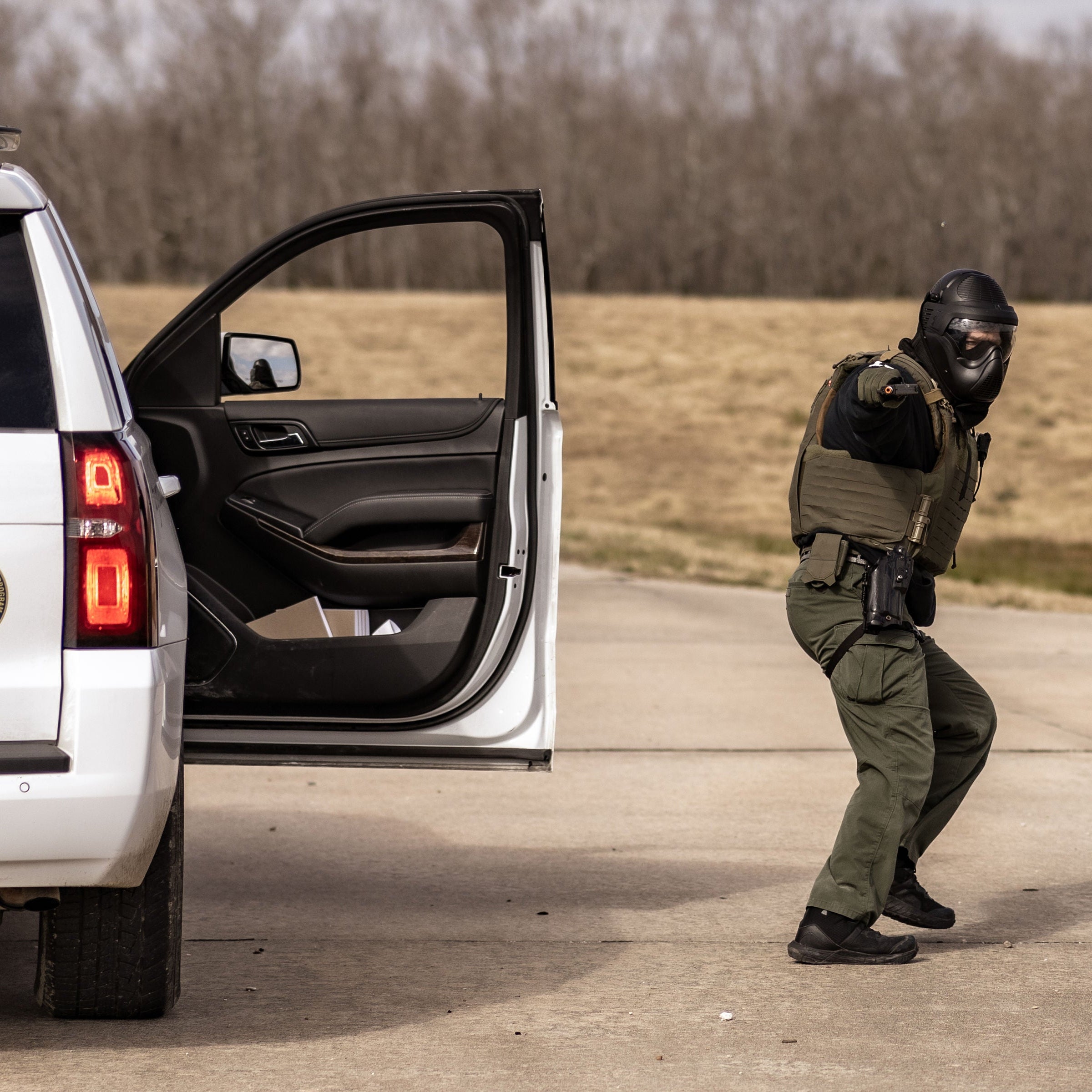 Person in tactical gear standing next to a police vehicle with open door.